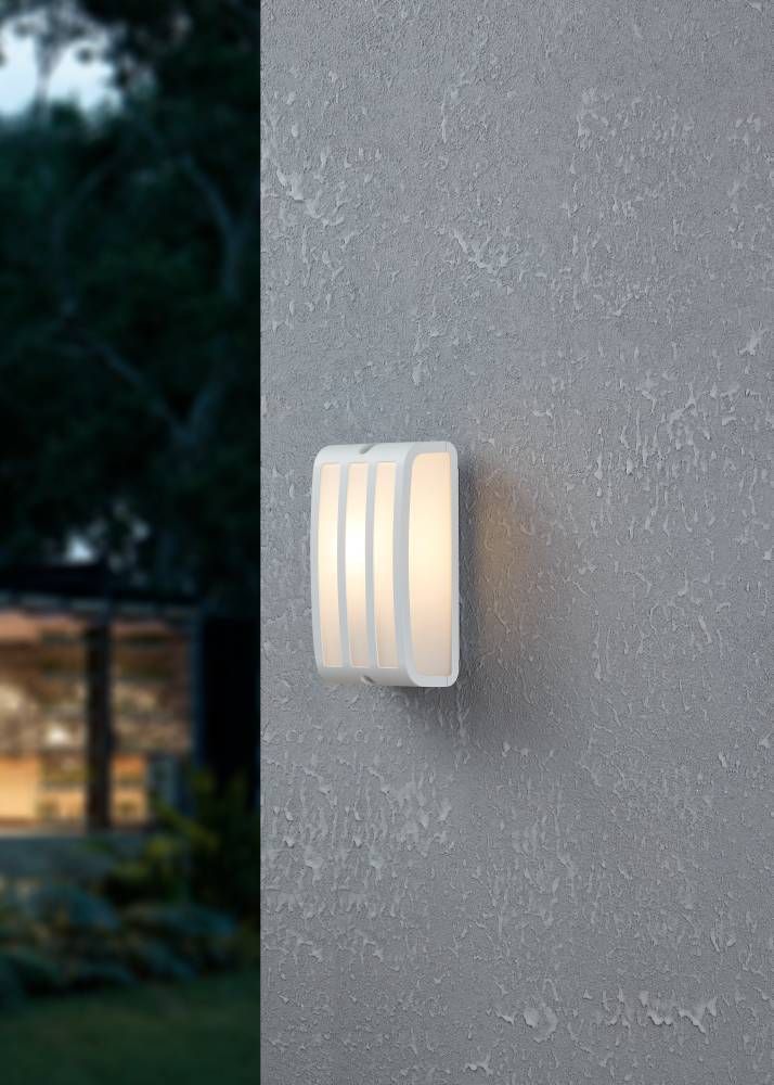 Applique murale allumée fixée sur un mur gris, ambiance de jardin au crépuscule
