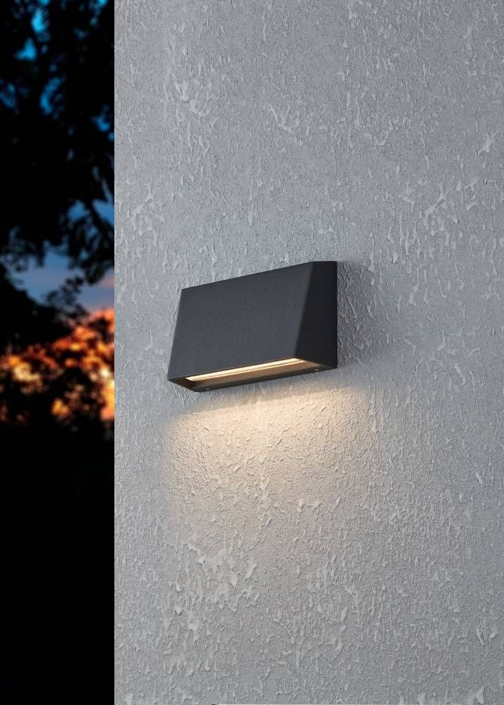 Applique murale extérieure noire allumée sur un mur crépi, lumière dirigée vers le bas