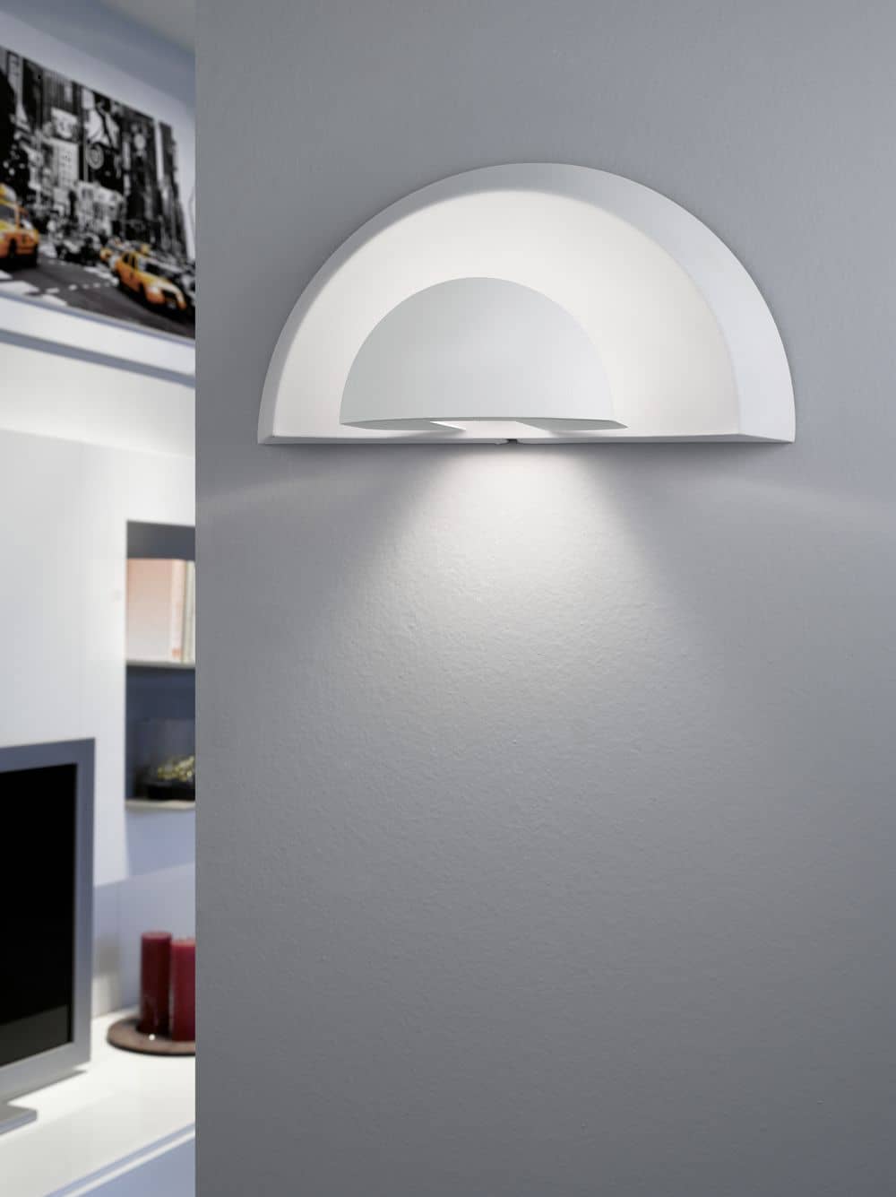 Mise en ambiance salon moderne, applique allumée diffusant une lumière rasante sur le mur gris