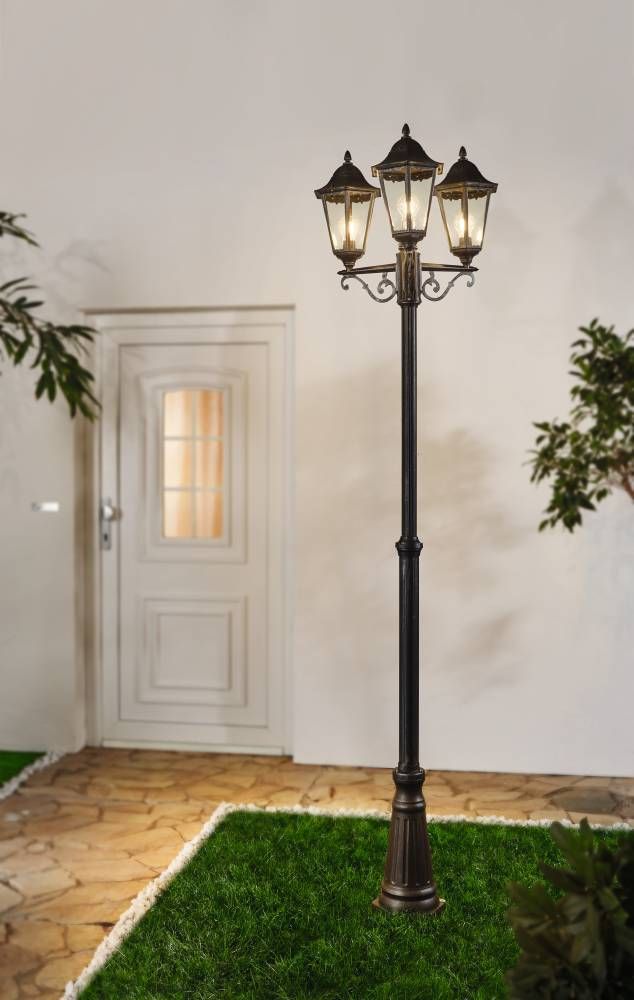 Lampadaire à trois lanternes allumées installé sur une pelouse devant une maison