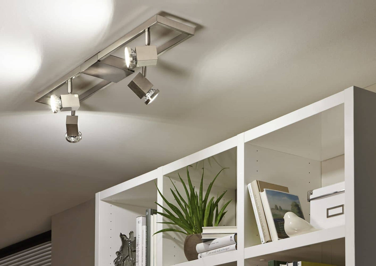 Mise en ambiance du spot plafond éclairant une étagère blanche avec plantes et livres.