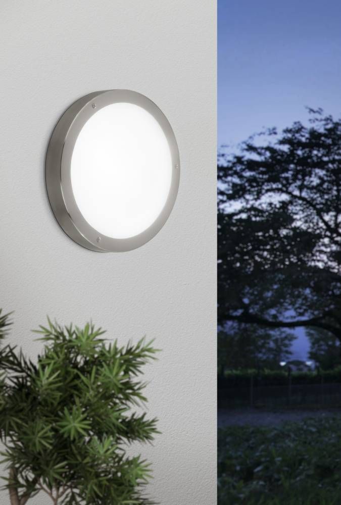 Applique ronde allumée fixée sur un mur blanc près d'un arbuste
