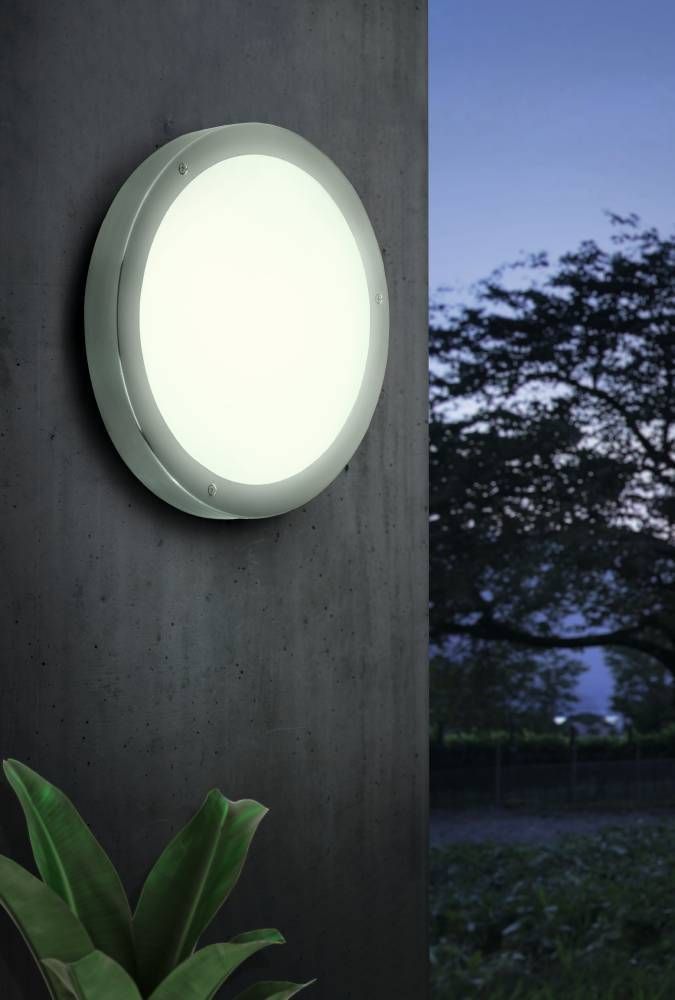 Luminaire mural extérieur allumé sur un mur béton gris en soirée