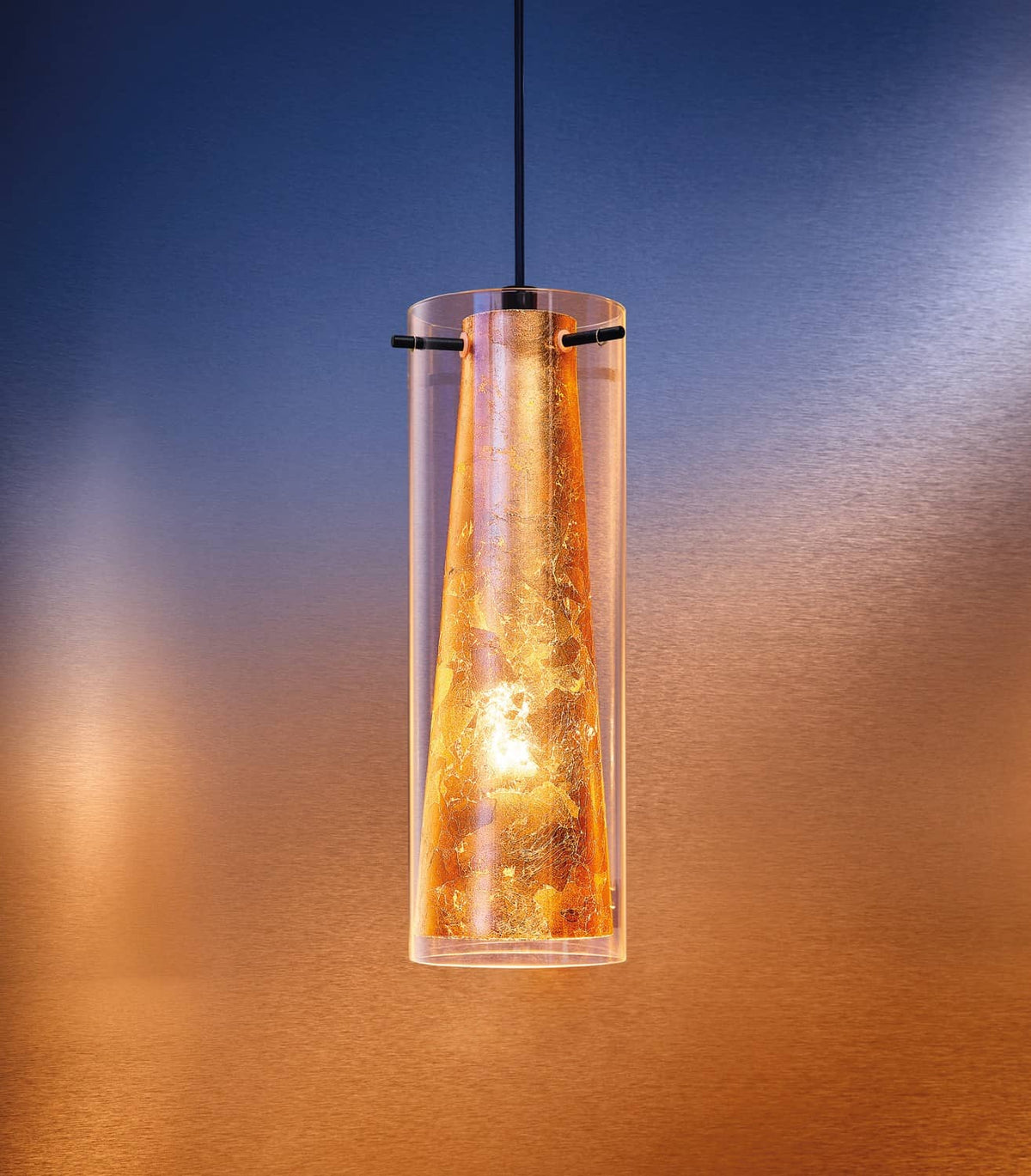 Gros plan en ambiance du luminaire allumé, abat-jour verre transparent et intérieur doré texturé.