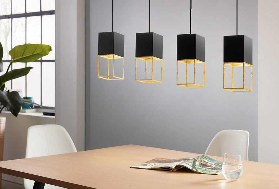Suspension à quatre cubes noirs et dorés éclairant une table en bois avec chaises blanches.