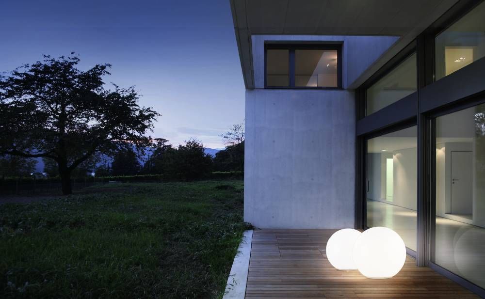 Deux sphères lumineuses blanches éclairant une terrasse en bois devant une maison moderne.
