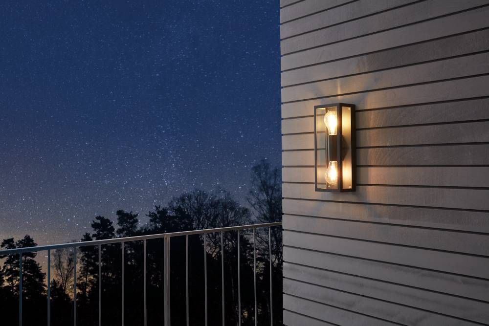 Vue rapprochée de l'applique murale noire éclairée sur bardage, ciel nocturne et rambarde.