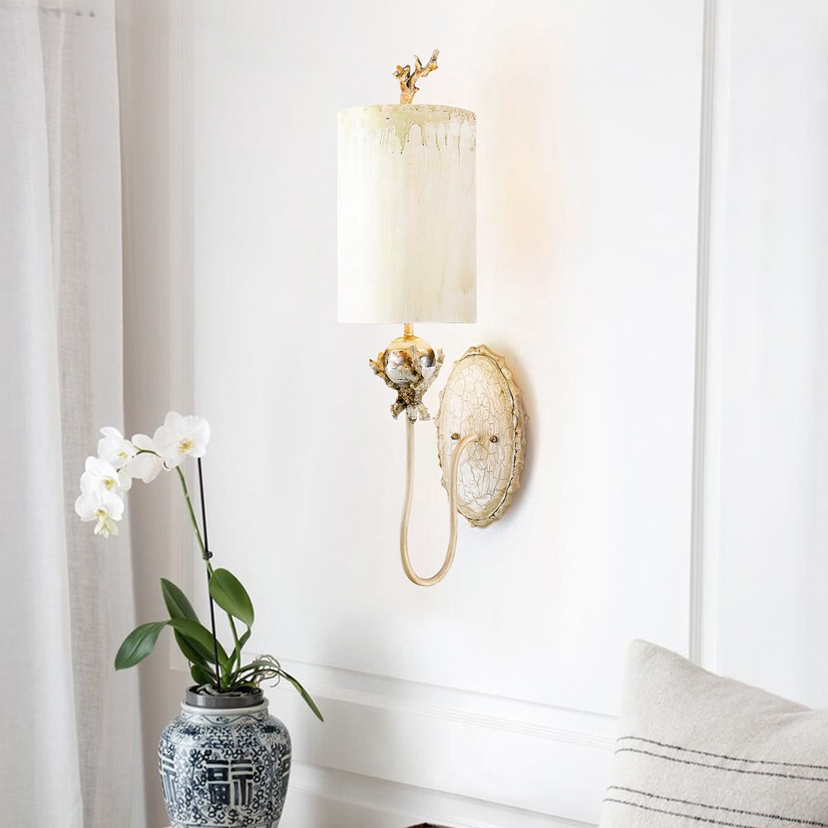 Mise en ambiance de l'applique allumée sur un mur blanc, orchidée et coussin