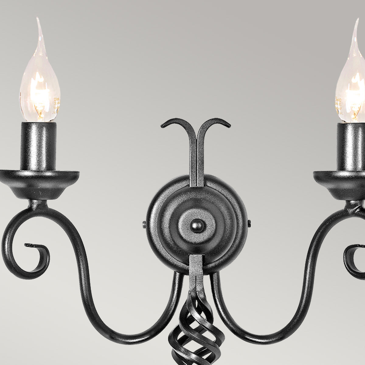 Détail des deux bras recourbés avec bougies et ampoules allumées sur fond gris.
