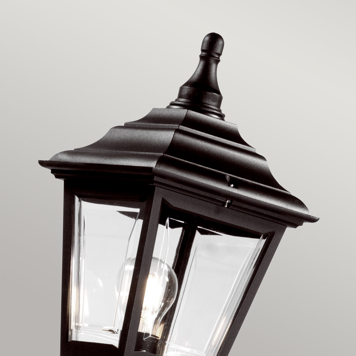 Gros plan du haut de lanterne noire, verre transparent, ampoule allumée et pommeau.