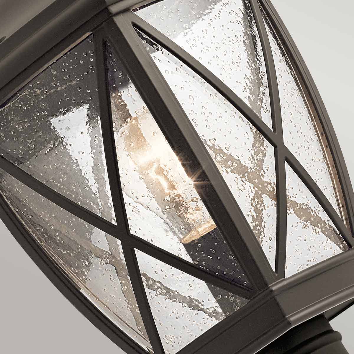 Gros plan sur le verre trempé et sa croix de bronze, ampoule allumée visible.