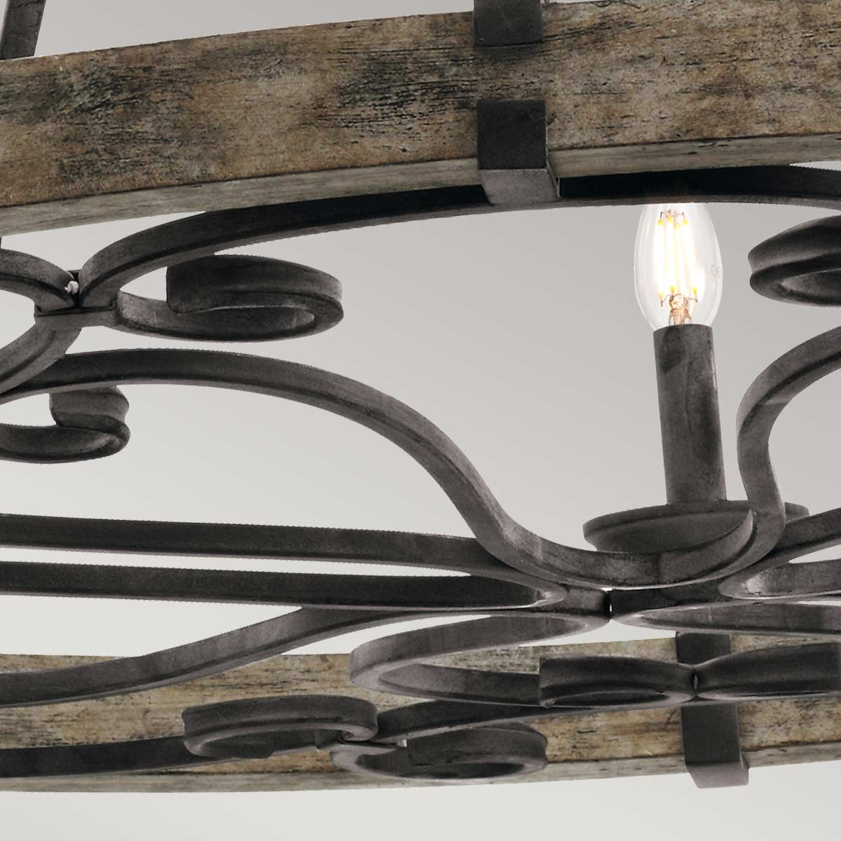 Détail du cercle en bois vieilli et des volutes en métal sombre sous le luminaire.