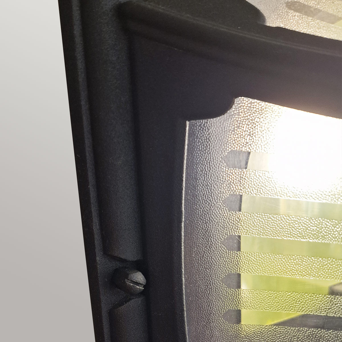 Détail de la vis de fixation sur cadre noir et verre strié éclairé.
