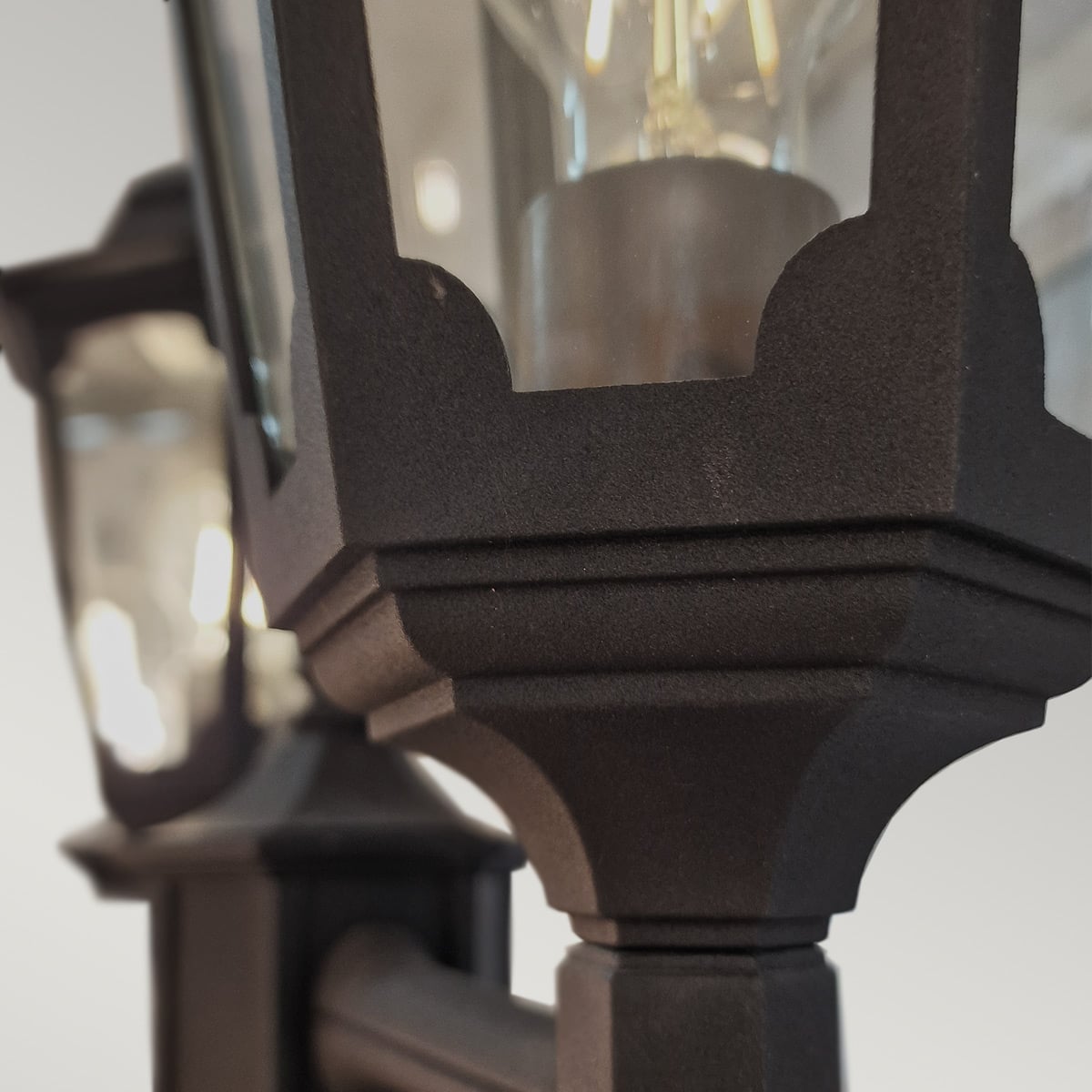 Détail d'une lanterne en verre avec ampoule visible et cadre noir.