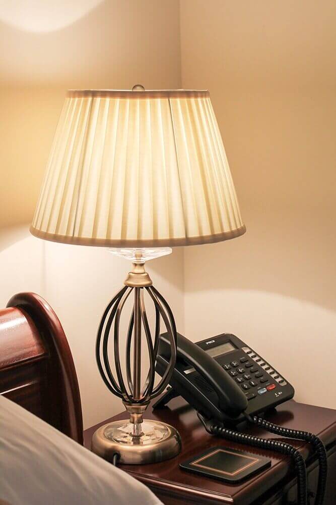 Lampe allumée posée sur une table de nuit en bois à côté d'un téléphone.