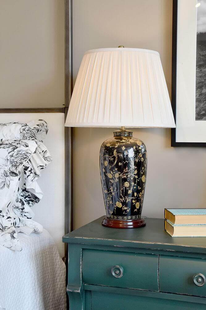 Lampe posée sur une commode verte dans une chambre, linge de lit fleuri