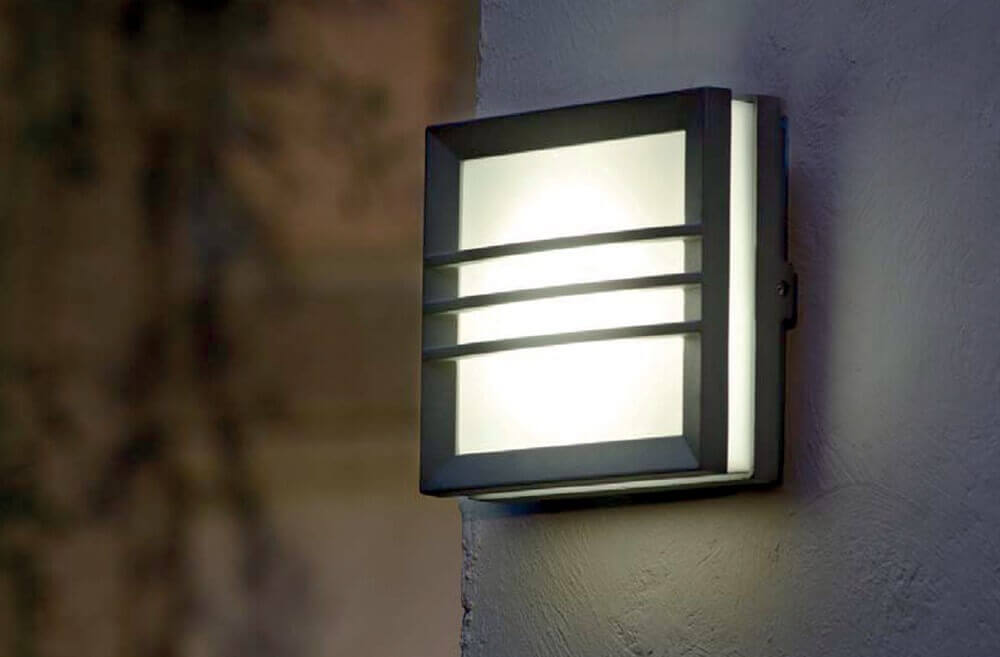 Applique murale carrée allumée sur un mur extérieur crème, halo lumineux diffus