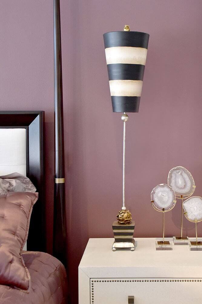 Mise en ambiance de la lampe posée sur une commode blanche, chambre aux murs mauves.
