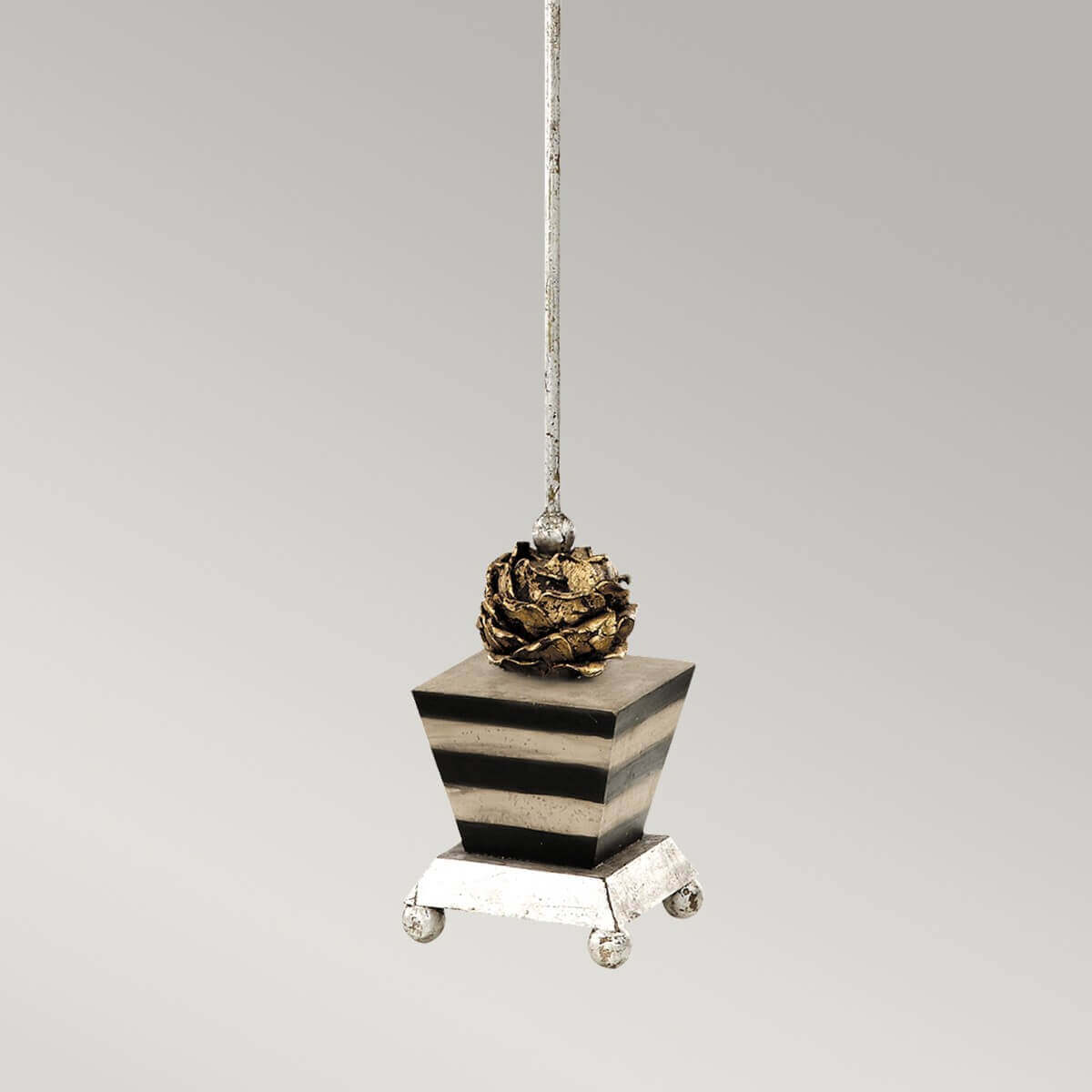 Détail du socle carré rayé, de la pomme de pin dorée et des pieds argentés.