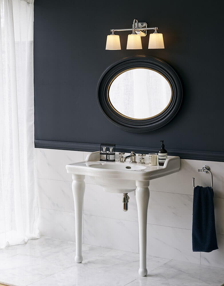 Applique allumée au-dessus d'un miroir ovale sur mur bleu nuit, ambiance raffinée.