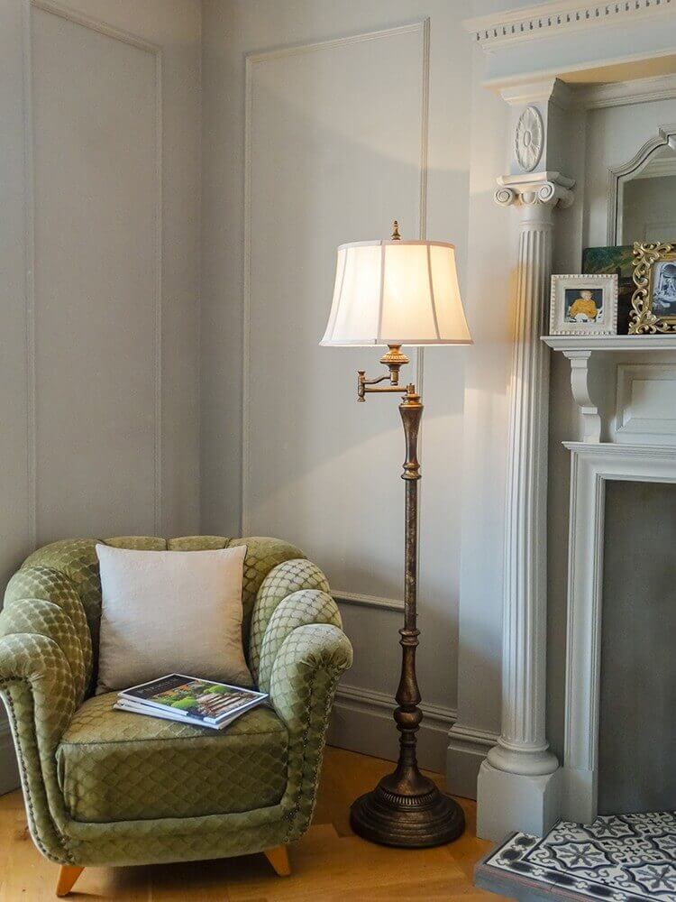 Lampadaire allumé près d'un fauteuil vert dans un salon à moulures