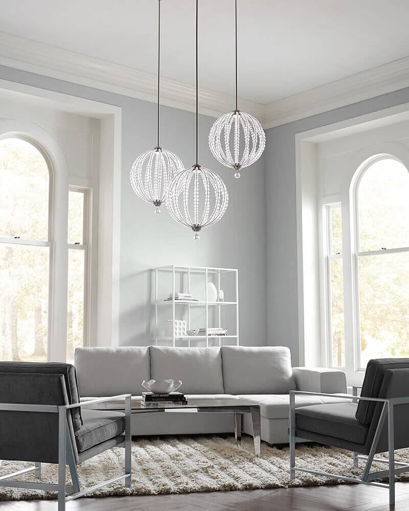 Trois suspensions cristal allumées dans un salon gris et blanc lumineux