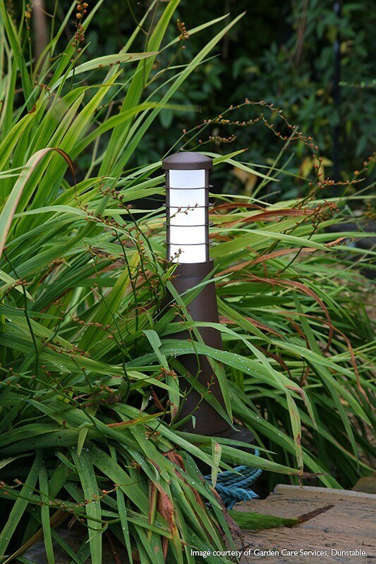 Borne lumineuse installée dans une bordure de graminées, éclairant le jardin
