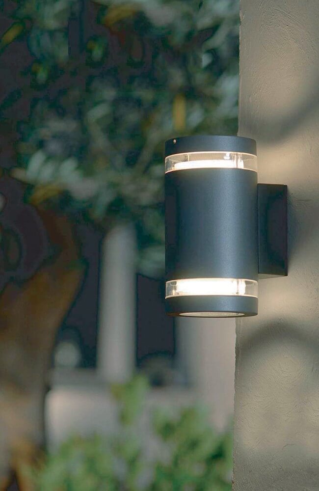Mise en ambiance nocturne de l'applique fixée sur un mur extérieur près du feuillage