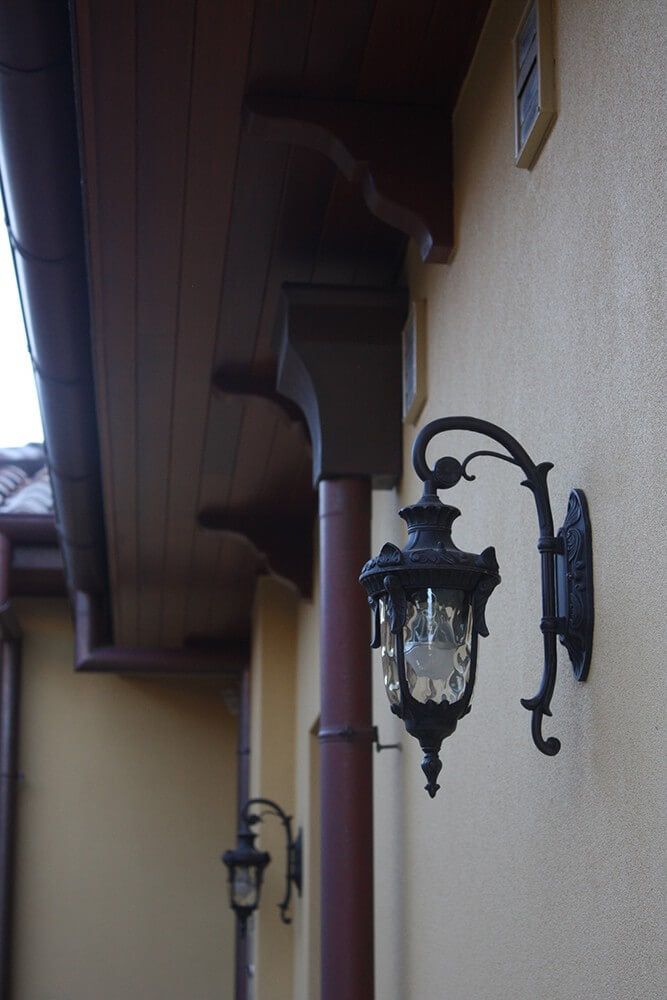 Applique extérieure noire fixée sous avancée de toit, autre luminaire en arrière-plan flou
