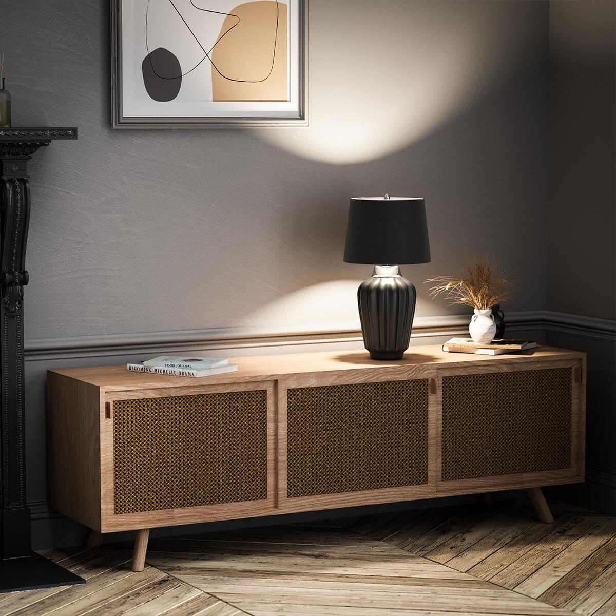 Mise en ambiance : lampe allumée posée sur un meuble en bois cannage.