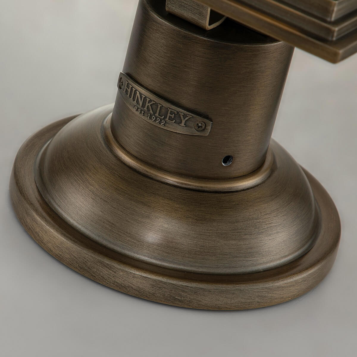 Détail de la base cylindrique bronze avec plaque estampée et embase circulaire.
