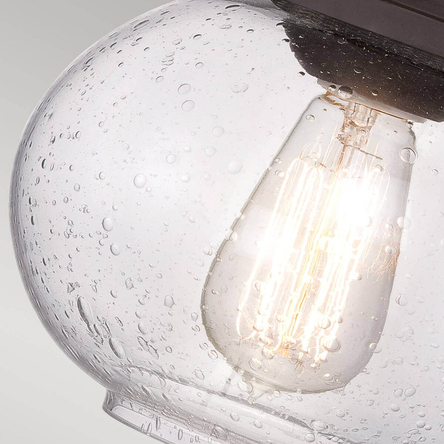 Gros plan du globe en verre bullé laissant voir l'ampoule à filament allumée.