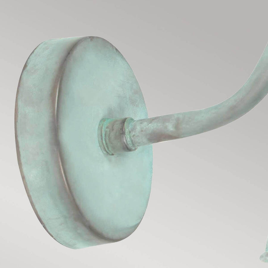Détail de la platine ronde fixée au mur et du bras métallique à patine verte