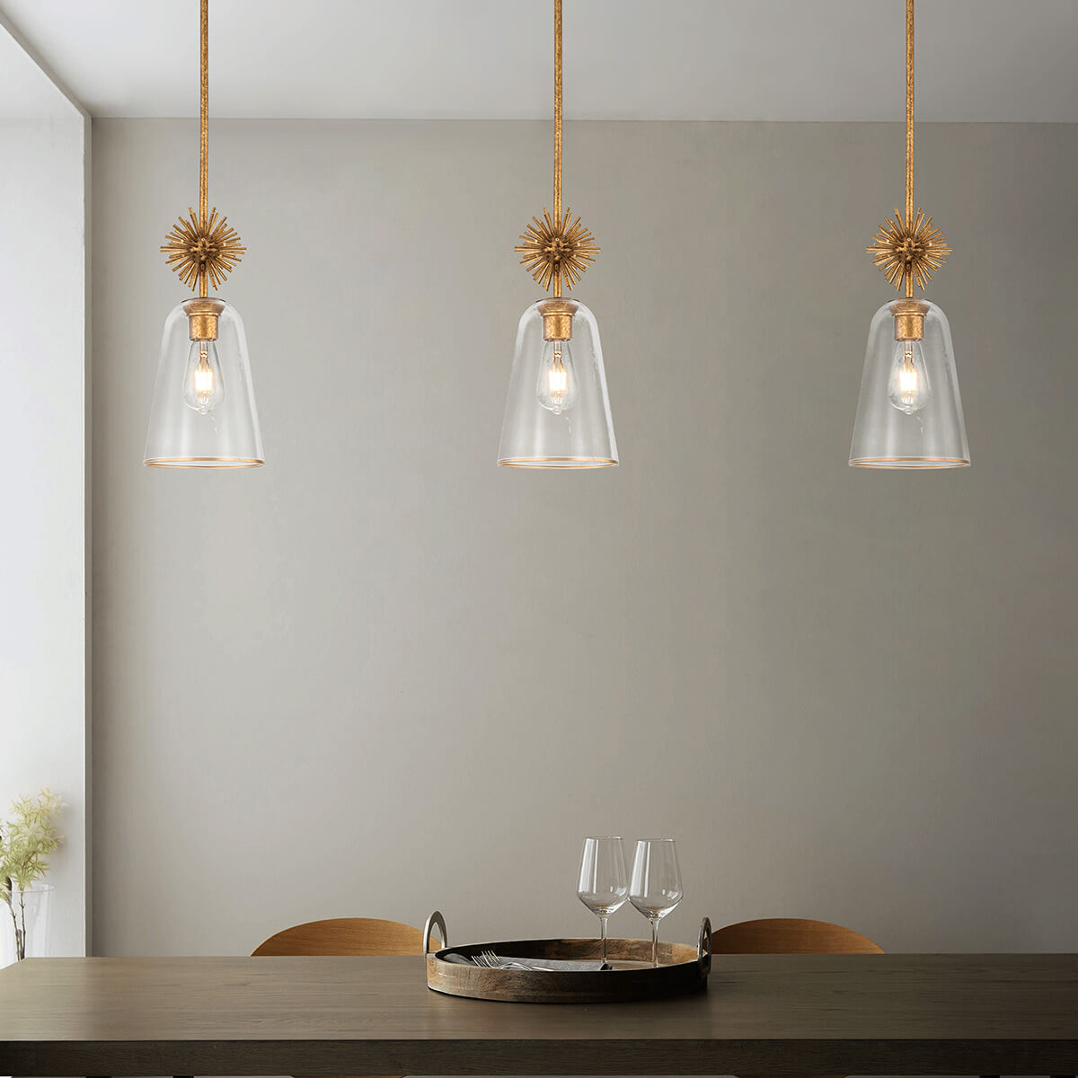 Mise en ambiance de trois suspensions dorées au-dessus d'une table avec plateau et verres.