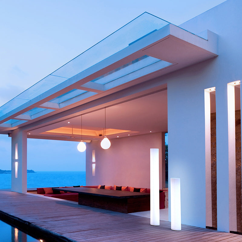 Terrasse en bois au crépuscule avec piscine, vue mer et deux lampadaires cylindriques allumés