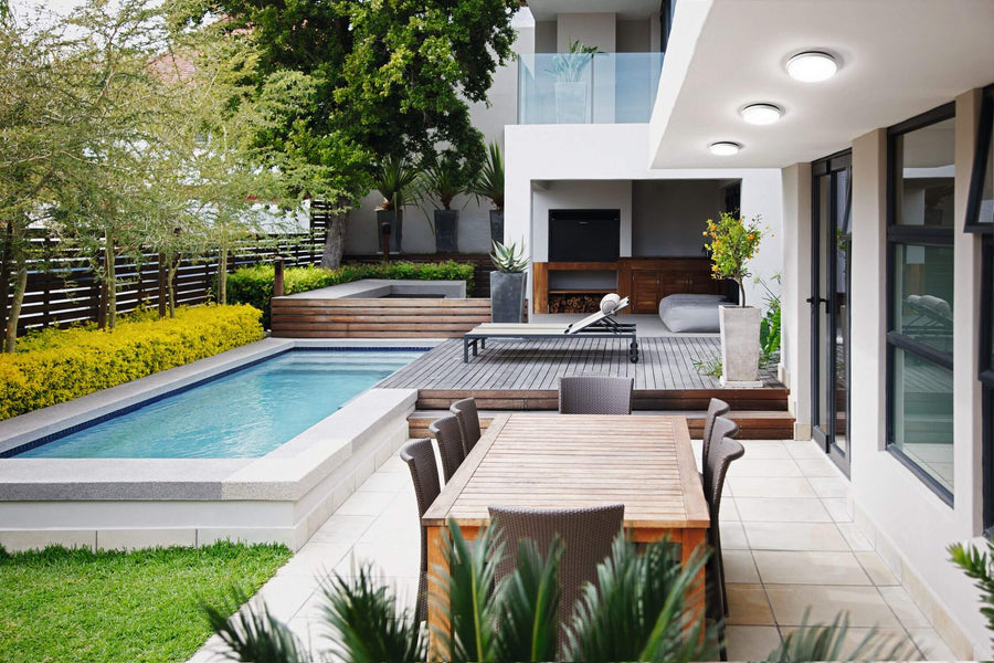 Trois plafonniers ronds noirs sous un soffite, terrasse avec piscine et mobilier extérieur