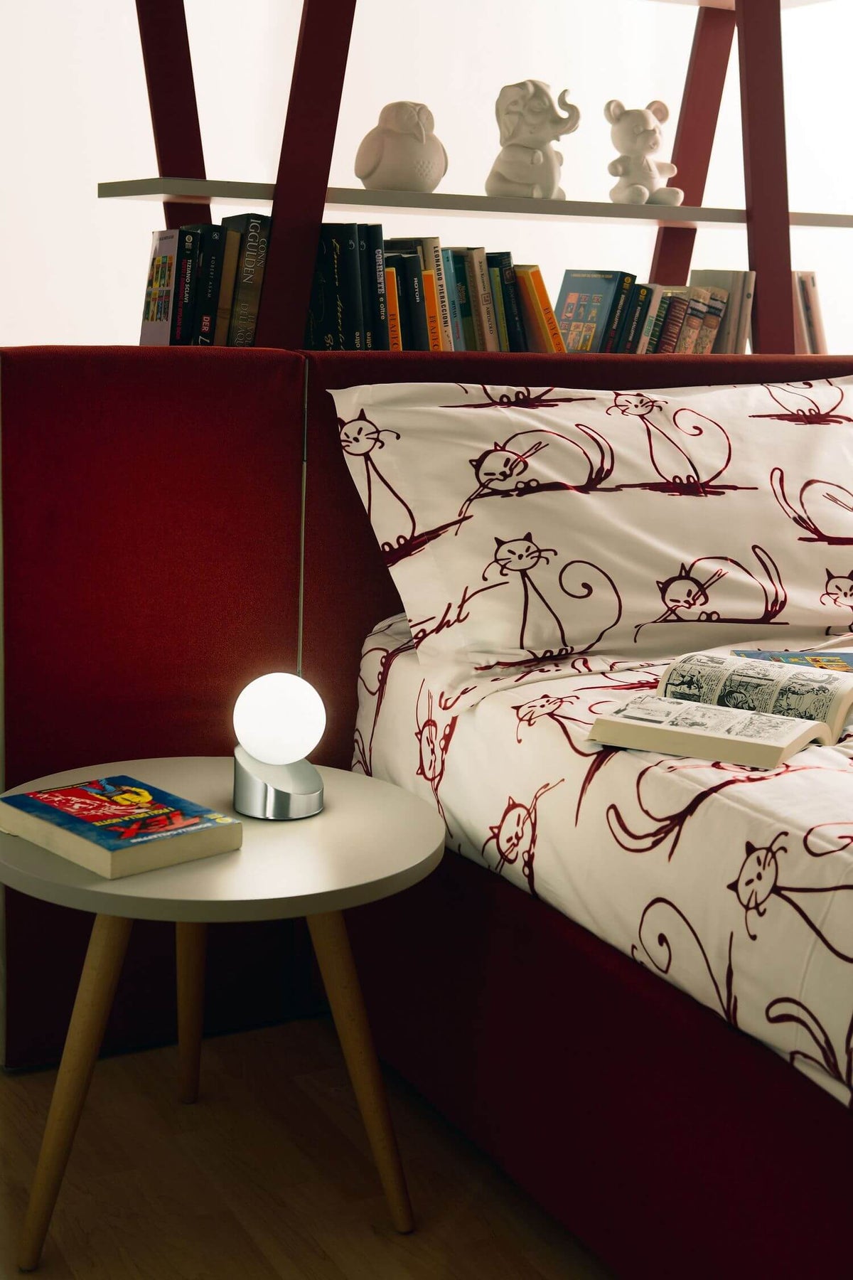 Lampe allumée sur table de chevet en bois, près d'un lit rouge dans une chambre