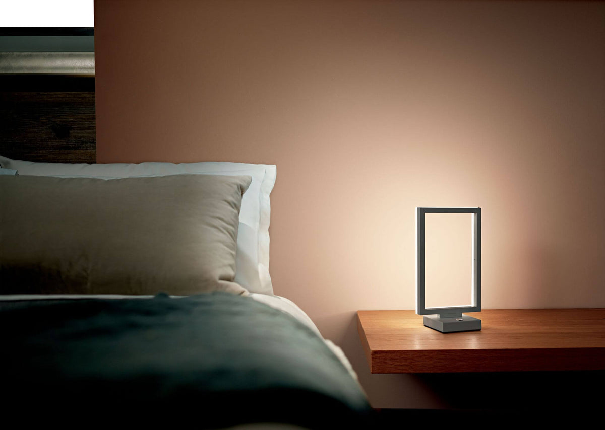 Mise en ambiance nocturne : lampe posée sur table de chevet en bois près du lit