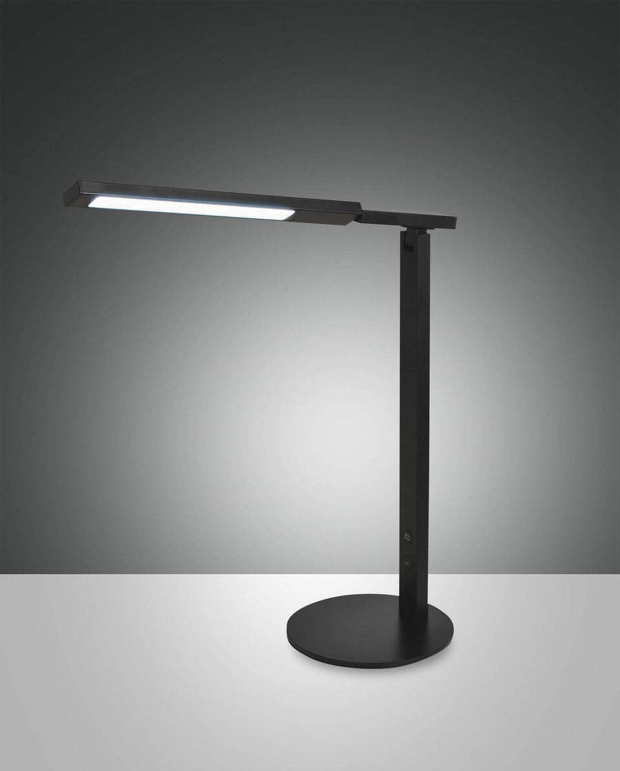 Lampe de bureau noire vue de trois quarts sur fond gris dégradé, tête allumée.