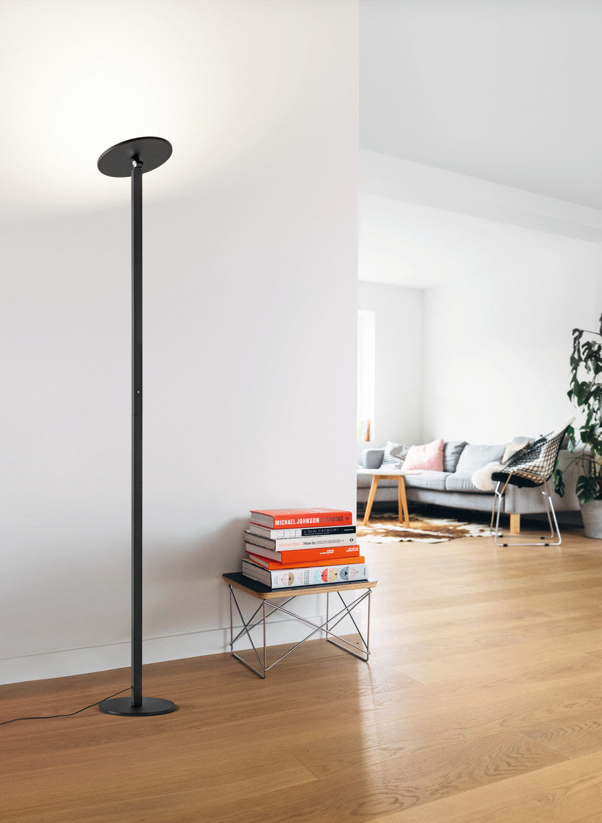 Mise en ambiance salon clair, lampadaire posé au sol près d'une pile de livres