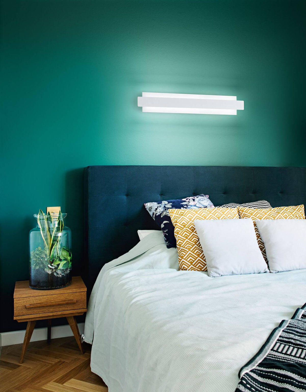 Ambiance chambre avec applique murale allumée au-dessus d'une tête de lit bleu nuit