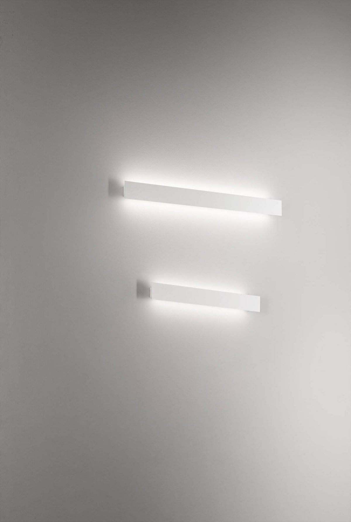 Deux appliques fines allumées côte à côte, halo lumineux sur mur blanc clair