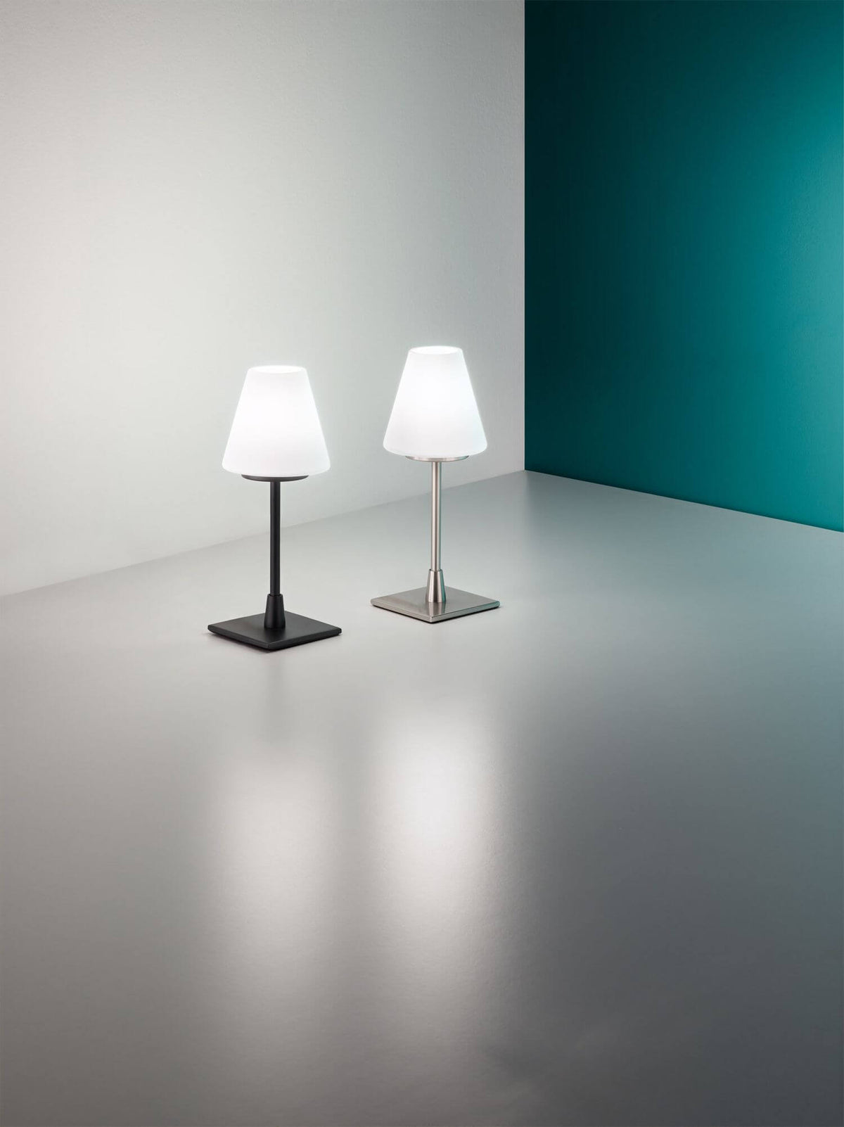Deux lampes identiques, versions noire et acier, éclairées dans un décor minimaliste