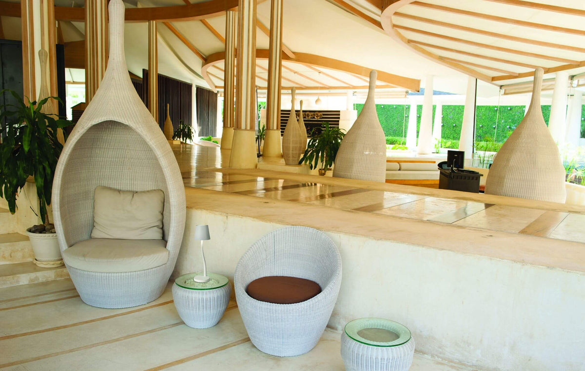 Mise en ambiance extérieure, lampe posée sur table basse près de fauteuils tressés