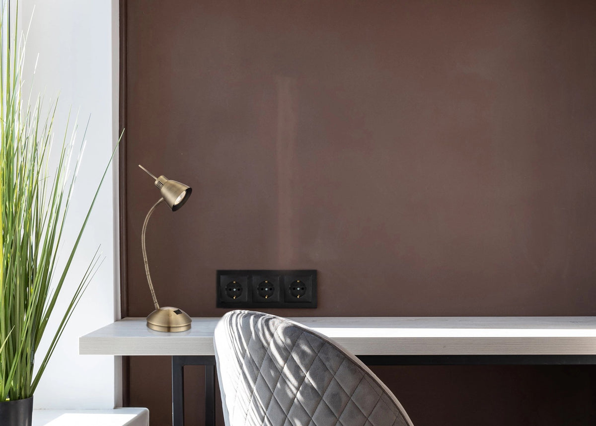 Lampe de bureau en laiton sur un plan de travail en bois devant un mur marron.