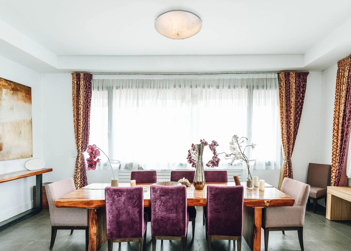 Mise en ambiance d'une salle à manger avec le plafonnier allumé au-dessus d'une table en bois.