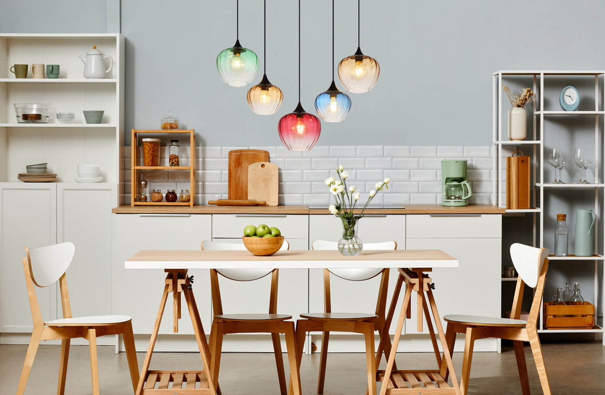 Mise en scène dans une cuisine, suspensions colorées au-dessus d'une table en bois clair.