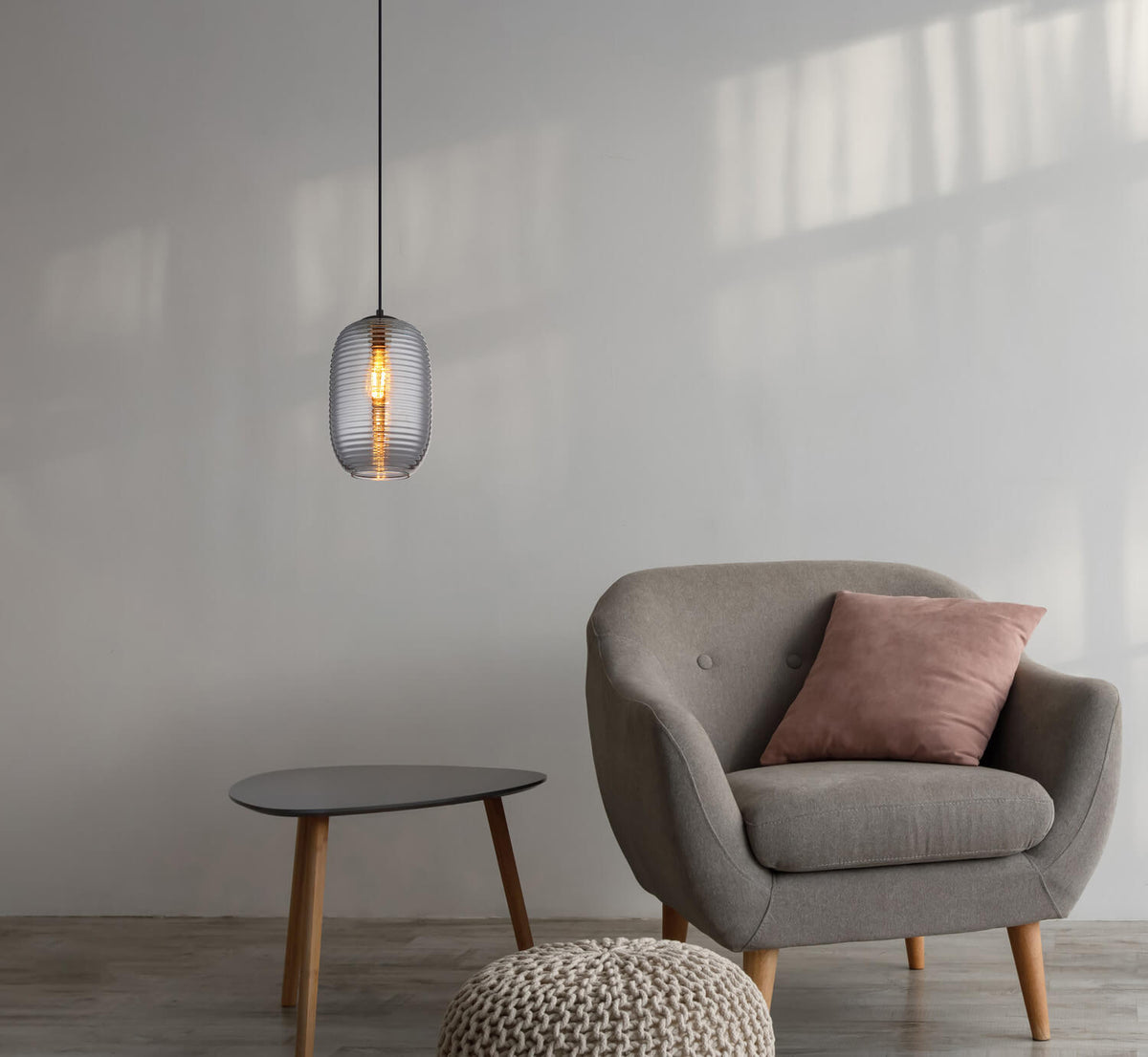 Mise en ambiance : suspension éclairée au-dessus d'un fauteuil gris et petite table.