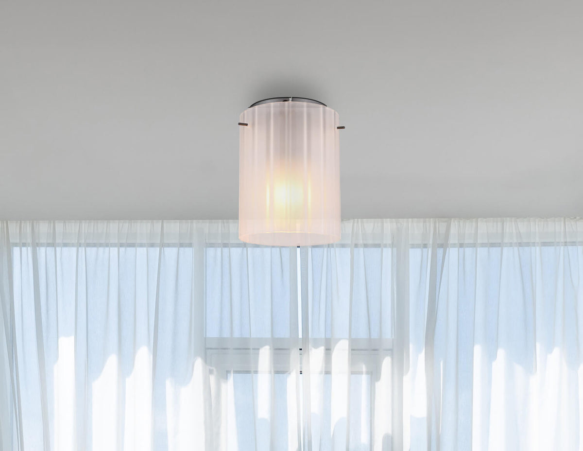 Mise en ambiance : luminaire fixé au plafond devant des rideaux voilages blancs lumineux