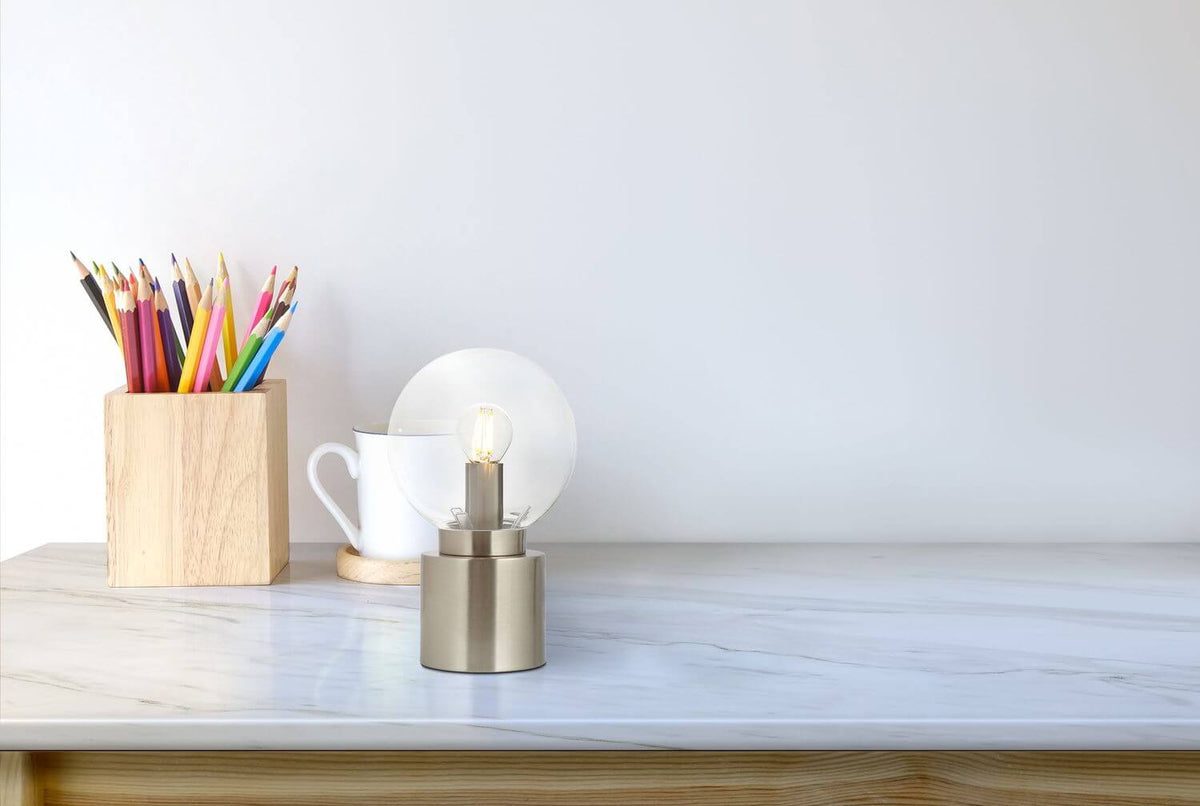Mise en ambiance sur un bureau, lampe allumée près d'un pot à crayons et d'une tasse.